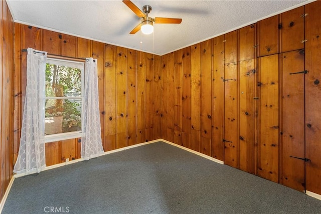 carpeted empty room with ceiling fan, wood walls, and a textured ceiling