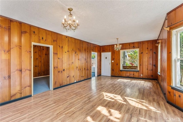 spare room featuring a textured ceiling, baseboards, wood finished floors, and a notable chandelier