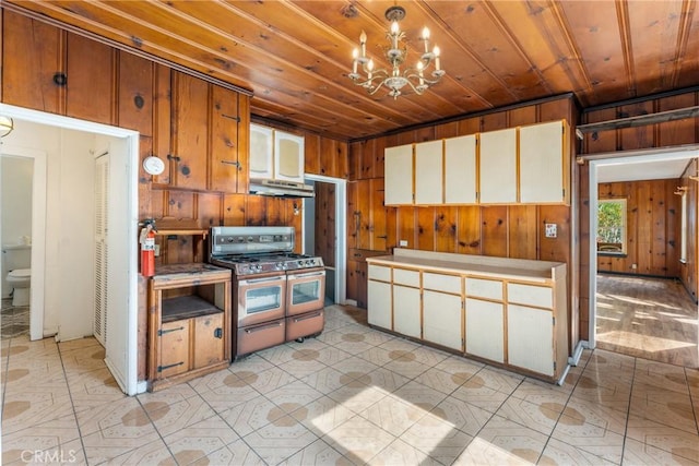 kitchen with wooden ceiling, under cabinet range hood, wooden walls, double oven range, and an inviting chandelier