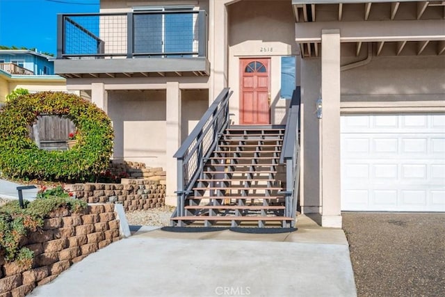 entrance to property with a garage, a balcony, and stucco siding