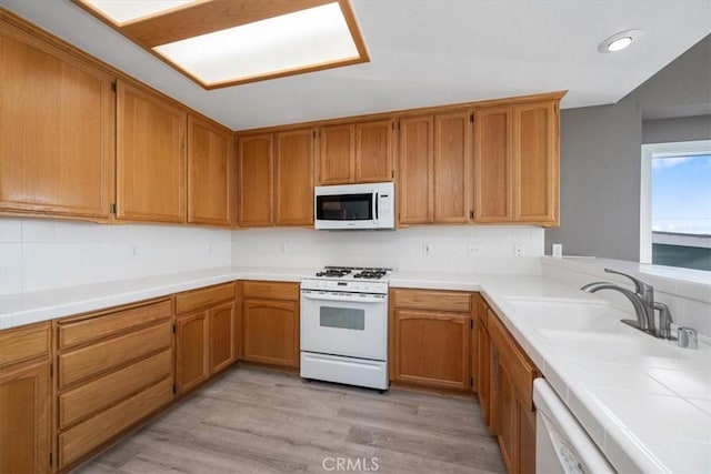 kitchen featuring tile counters, backsplash, light wood-style floors, a sink, and white appliances