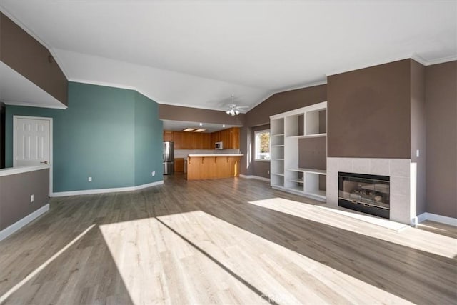 unfurnished living room with lofted ceiling, a fireplace, wood finished floors, baseboards, and crown molding