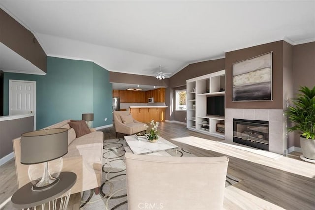 living area featuring crown molding, a fireplace, lofted ceiling, light wood-type flooring, and baseboards