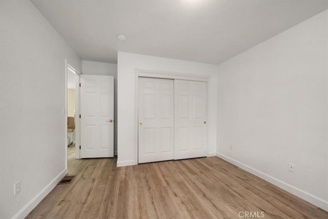 unfurnished bedroom with a closet, light wood-type flooring, visible vents, and baseboards