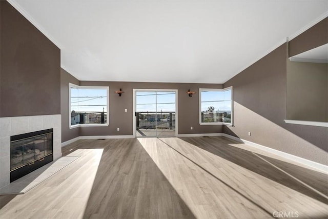 unfurnished living room featuring crown molding, lofted ceiling, wood finished floors, a tile fireplace, and baseboards