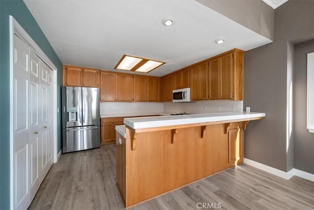 kitchen with stainless steel fridge, white microwave, a peninsula, light countertops, and light wood-type flooring