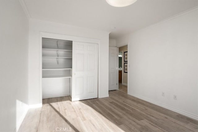 unfurnished bedroom with crown molding, a closet, baseboards, and wood finished floors