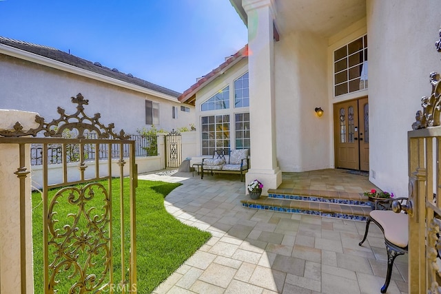 view of exterior entry featuring french doors, fence, and stucco siding