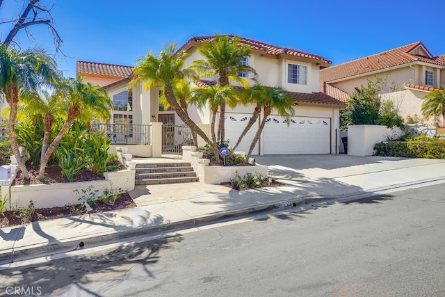 mediterranean / spanish-style house with a garage, concrete driveway, a tile roof, and stucco siding