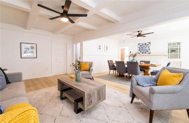 living area with coffered ceiling, a ceiling fan, baseboards, beam ceiling, and light wood finished floors