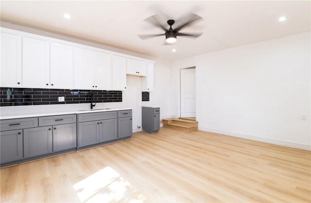 kitchen with gray cabinetry, a sink, a ceiling fan, light wood-style floors, and tasteful backsplash