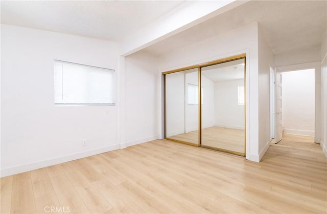 unfurnished bedroom with light wood-style floors, baseboards, and a closet