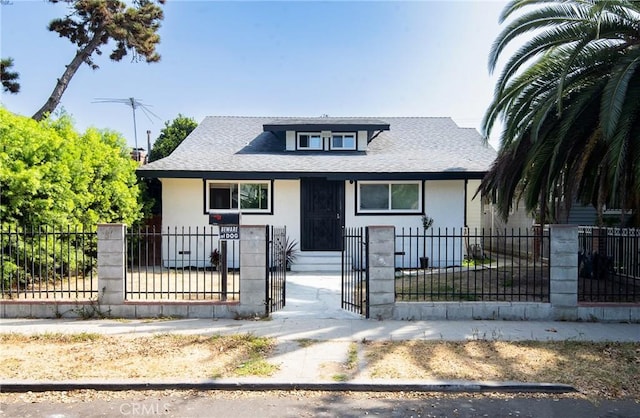 bungalow-style house with a shingled roof, a fenced front yard, and stucco siding