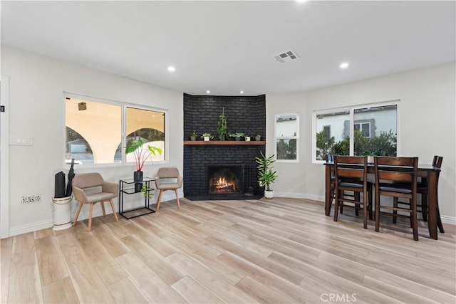 living area with light wood finished floors, recessed lighting, visible vents, a brick fireplace, and baseboards