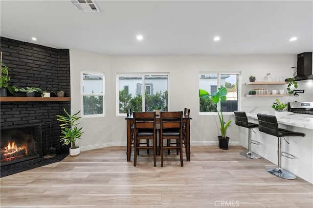 dining room featuring light wood-style floors, baseboards, a fireplace, and visible vents