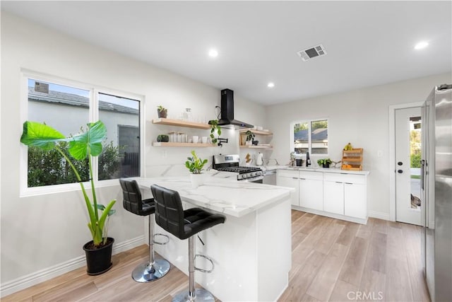 kitchen featuring visible vents, white cabinets, wall chimney exhaust hood, open shelves, and stainless steel range with gas stovetop