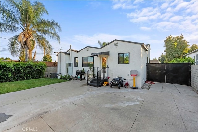 back of property with central AC, fence, a gate, and stucco siding