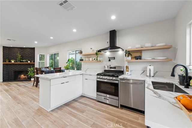 kitchen with island range hood, a peninsula, a sink, white cabinets, and appliances with stainless steel finishes