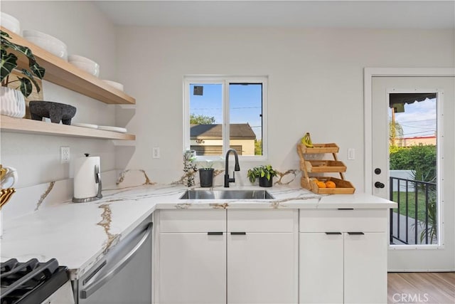 kitchen featuring stainless steel dishwasher, a sink, light stone counters, and white cabinets