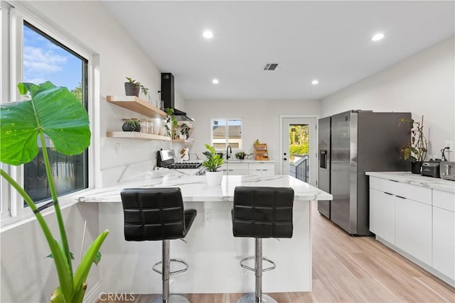 kitchen featuring a breakfast bar area, open shelves, appliances with stainless steel finishes, white cabinetry, and a peninsula