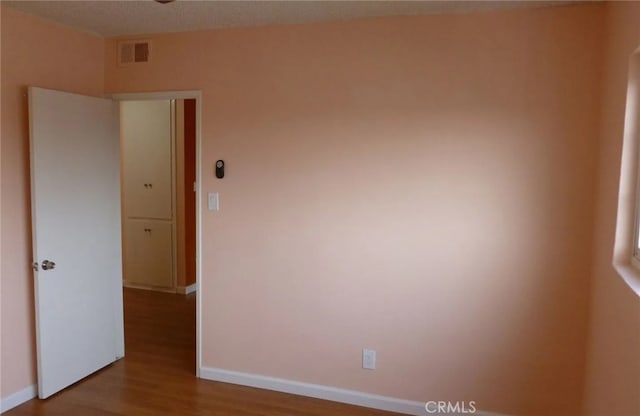 unfurnished room with wood finished floors, visible vents, and baseboards