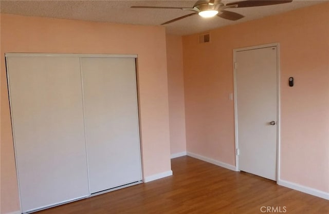 unfurnished bedroom with a textured ceiling, wood finished floors, visible vents, baseboards, and a closet