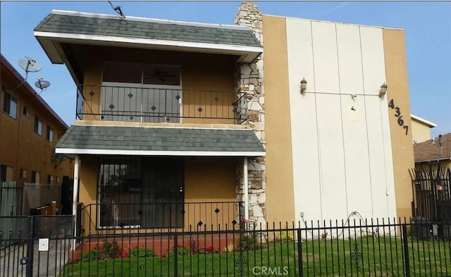 view of front of house with a balcony, a fenced front yard, a shingled roof, and stucco siding