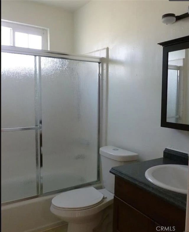 bathroom featuring toilet, shower / bath combination with glass door, and vanity