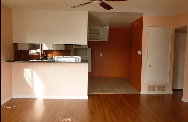 kitchen featuring a peninsula, dark countertops, visible vents, and wood finished floors