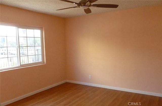 spare room featuring a textured ceiling, ceiling fan, wood finished floors, and baseboards