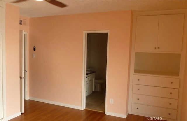 unfurnished bedroom with light wood-type flooring, baseboards, visible vents, and ensuite bath