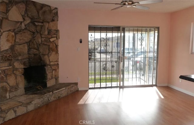 unfurnished living room with baseboards, a ceiling fan, wood finished floors, and a stone fireplace