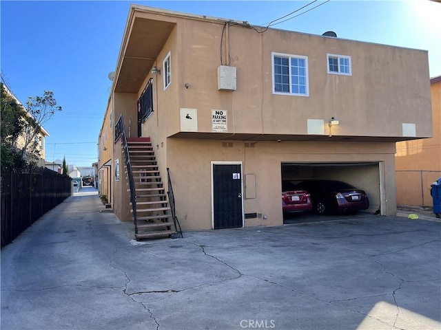 rear view of property with stucco siding, an attached garage, fence, driveway, and stairs