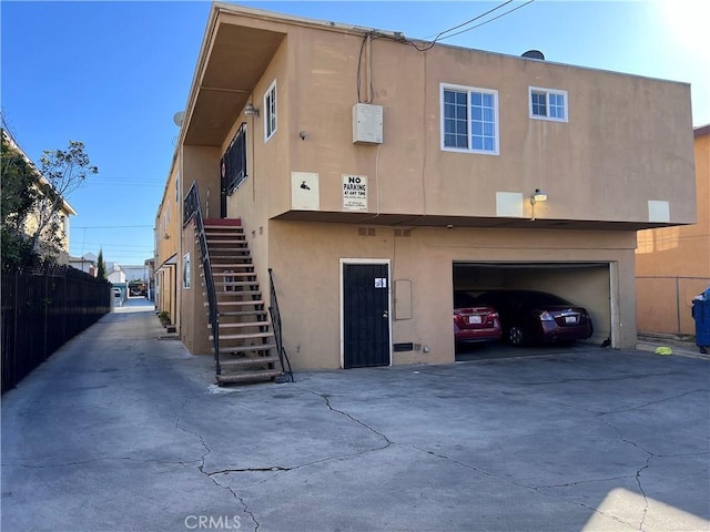 back of property with stucco siding, concrete driveway, stairway, an attached garage, and fence