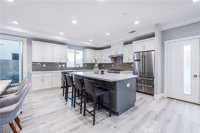 kitchen featuring light wood finished floors, white cabinets, a kitchen island, stainless steel appliances, and a kitchen bar