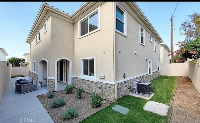 view of side of property featuring stone siding, a fenced backyard, central air condition unit, a patio area, and stucco siding