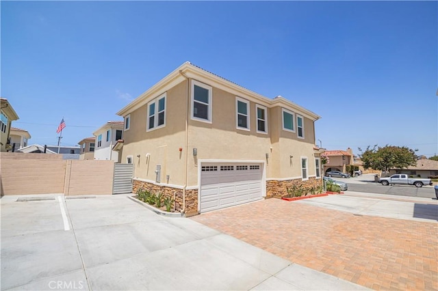 view of front of property featuring stone siding, a residential view, fence, decorative driveway, and stucco siding