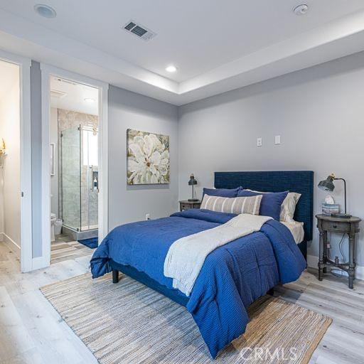 bedroom featuring baseboards, a tray ceiling, visible vents, and wood finished floors