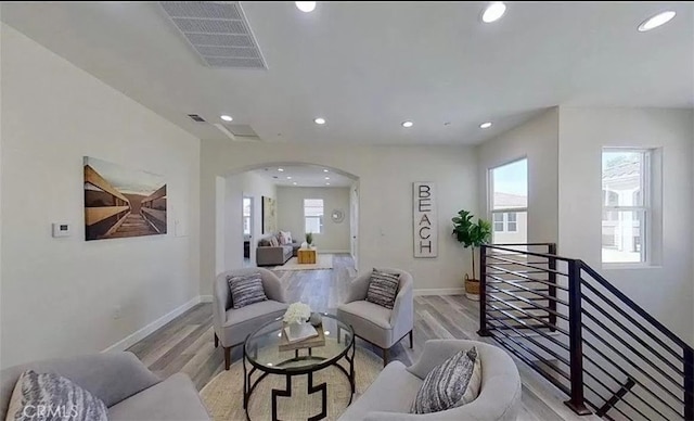 living area featuring arched walkways, light wood-style flooring, plenty of natural light, and visible vents