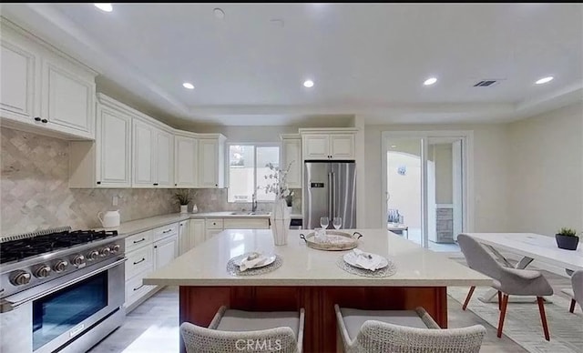 kitchen with a kitchen island, white cabinets, light countertops, decorative backsplash, and high end appliances