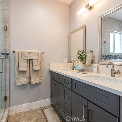 bathroom with a sink, a shower stall, baseboards, and double vanity