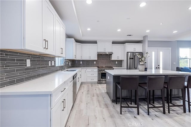 kitchen with premium appliances, a sink, a kitchen island, a kitchen breakfast bar, and white cabinets