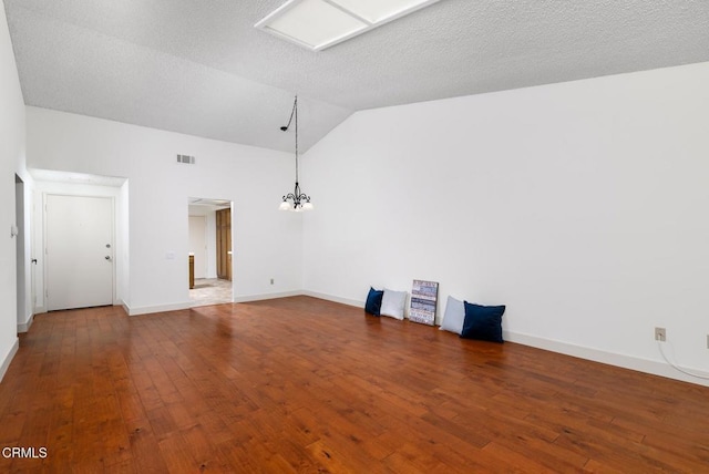 spare room featuring lofted ceiling, a textured ceiling, hardwood / wood-style flooring, visible vents, and baseboards