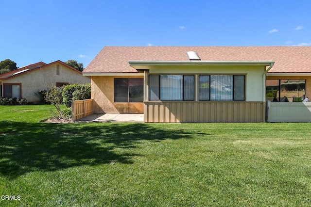 back of property with a yard, roof with shingles, fence, and stucco siding