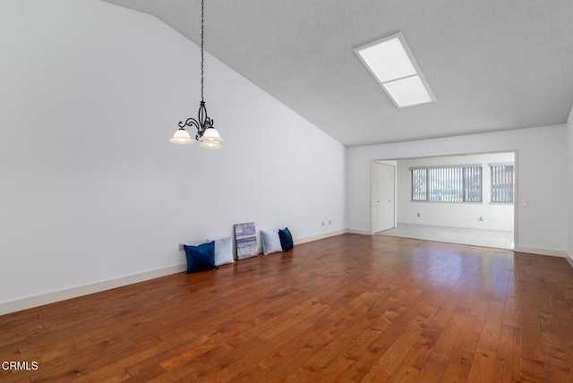 empty room with a chandelier, vaulted ceiling, baseboards, and hardwood / wood-style flooring