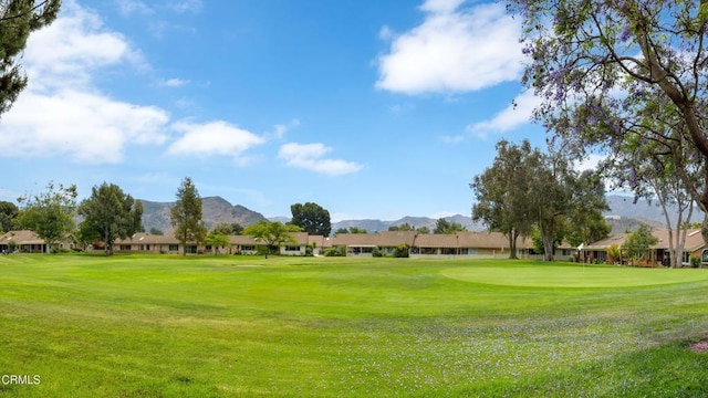 surrounding community with view of golf course, a yard, and a mountain view