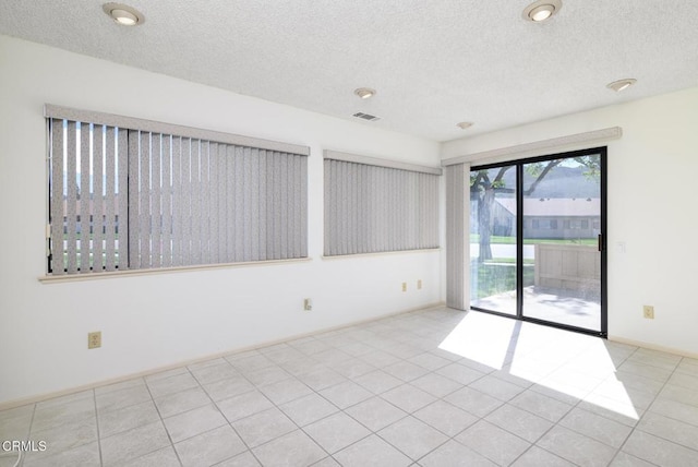 empty room featuring tile patterned flooring, baseboards, visible vents, and a textured ceiling