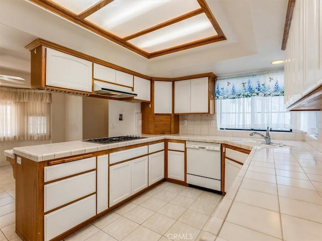 kitchen featuring white cabinets, tile countertops, a peninsula, white dishwasher, and a sink