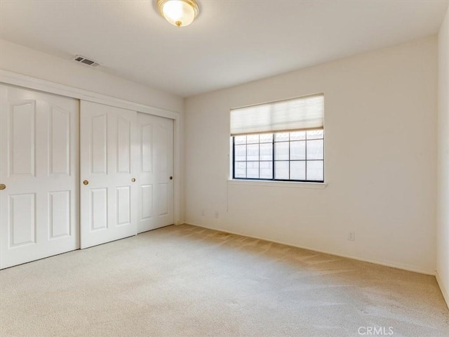 unfurnished bedroom featuring visible vents, a closet, and light colored carpet