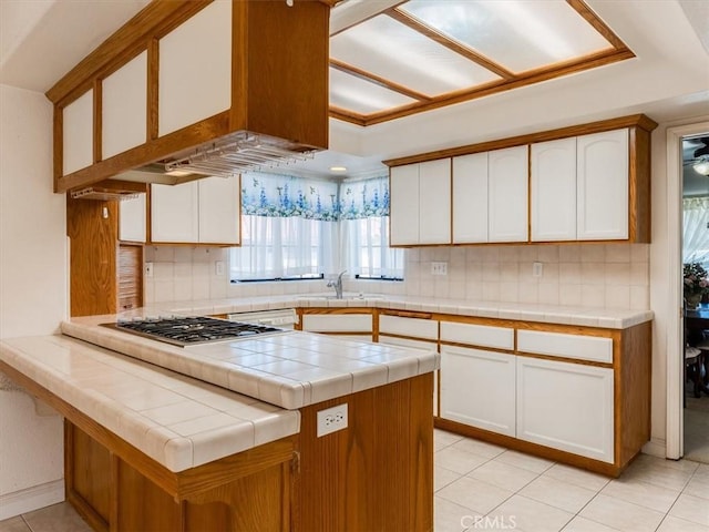 kitchen with tile countertops, a peninsula, stainless steel gas cooktop, and white cabinets